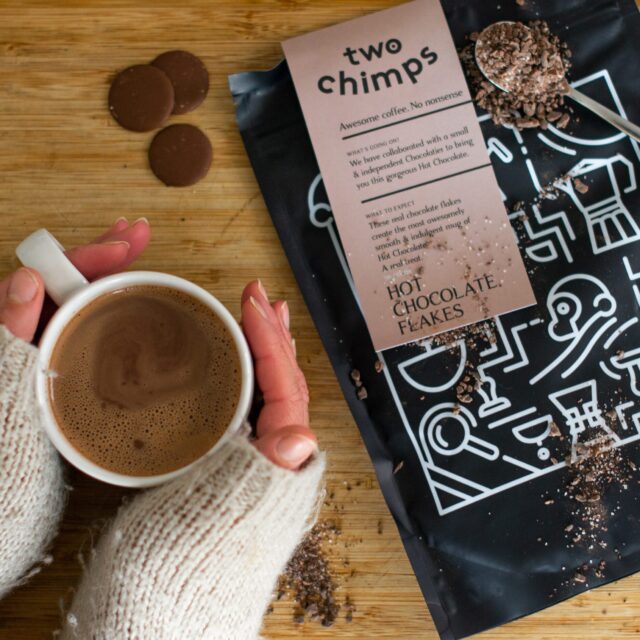 A person holding a hot mug of hot chocolate with some Two Chimps Hot Chocolate Flakes