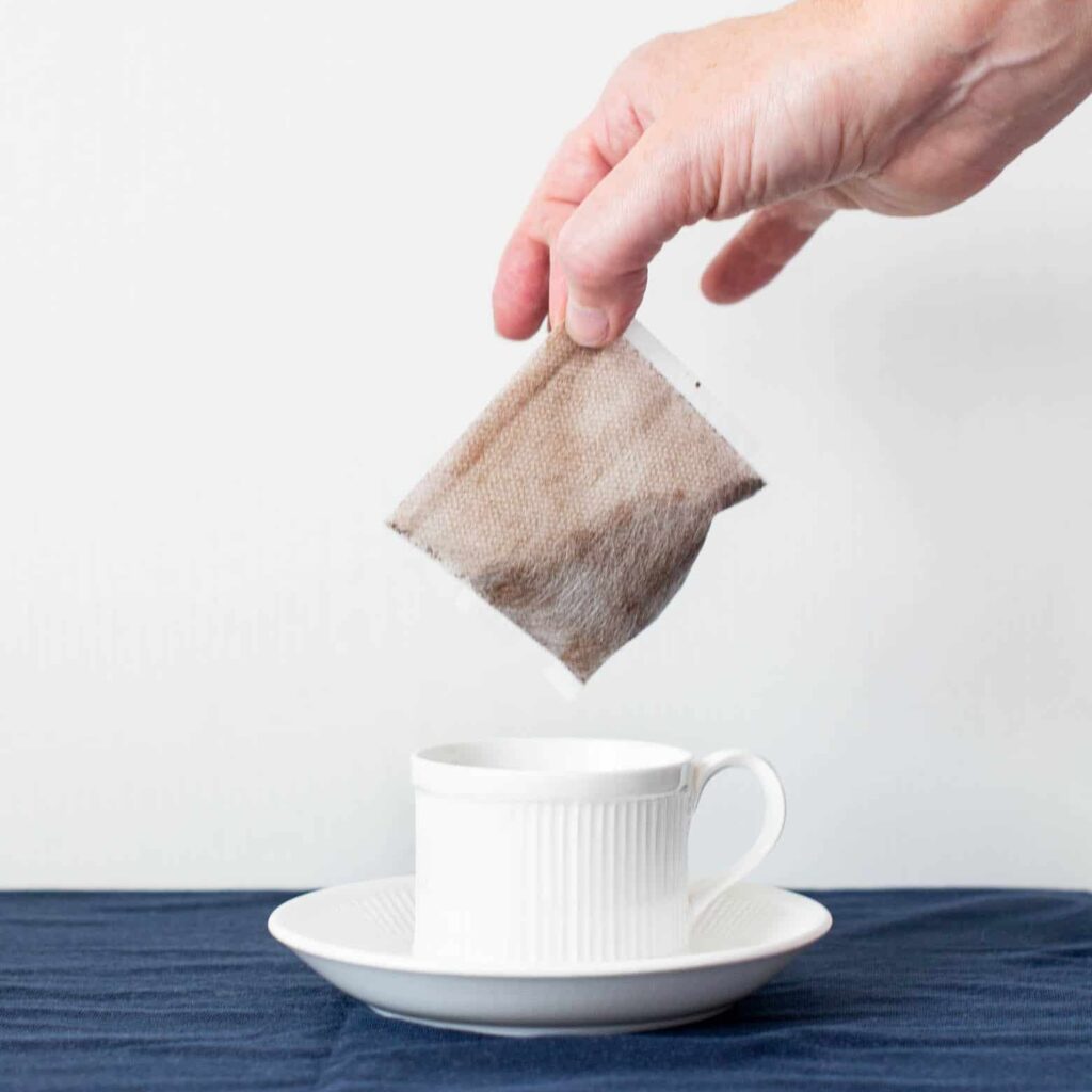 Close up of hand putting a coffee bag in a white teacup and saucer