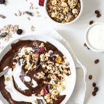 Coffee mocha smoothie in a white bowl with cups of granola and yoghurt and sprinkled with dried fruit