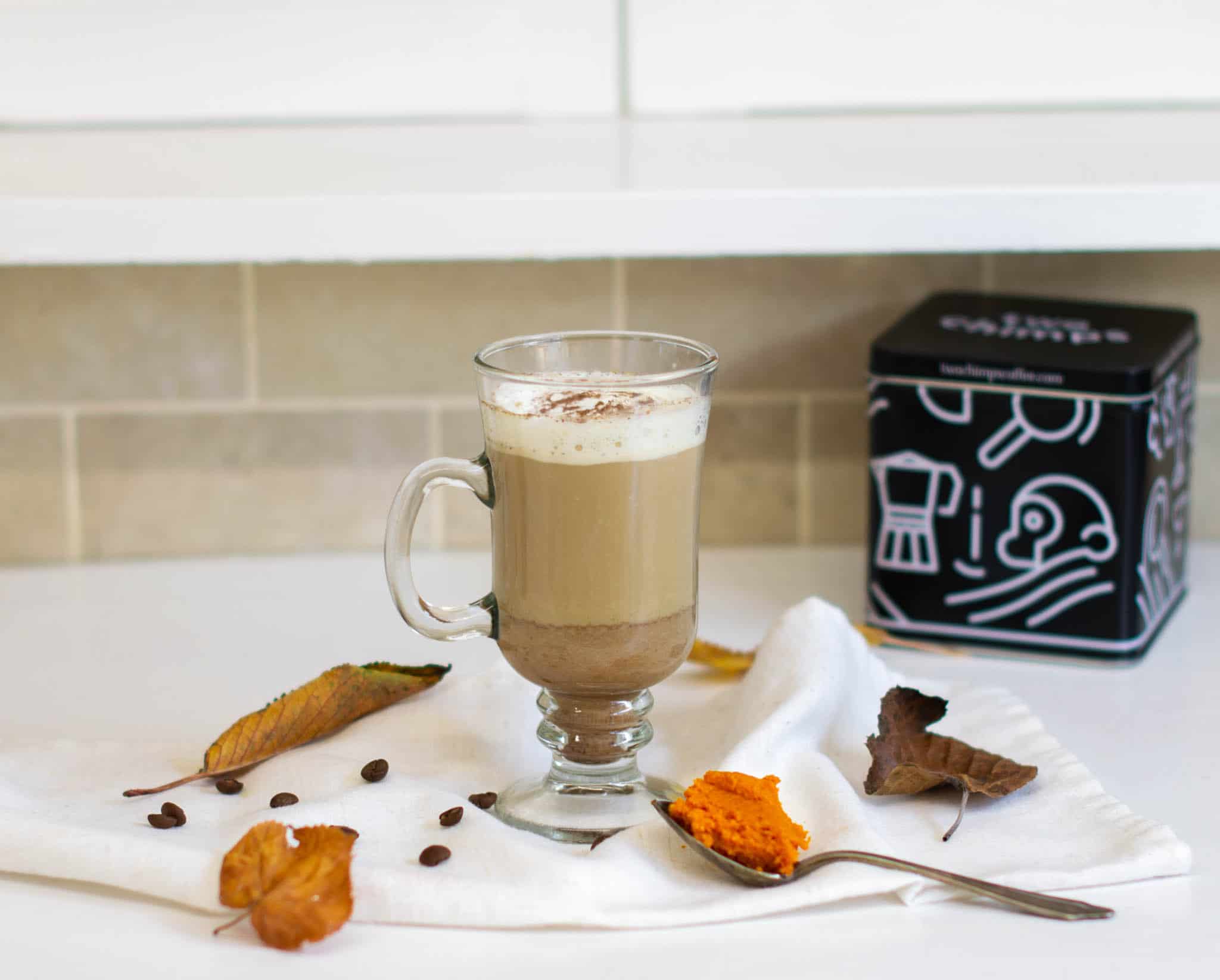 Pumpkin spice coffee beside Two Chimps coffee tin, teaspoon, leaves and coffee beans