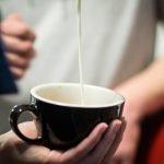 Pouring steamed milk into black latte cup