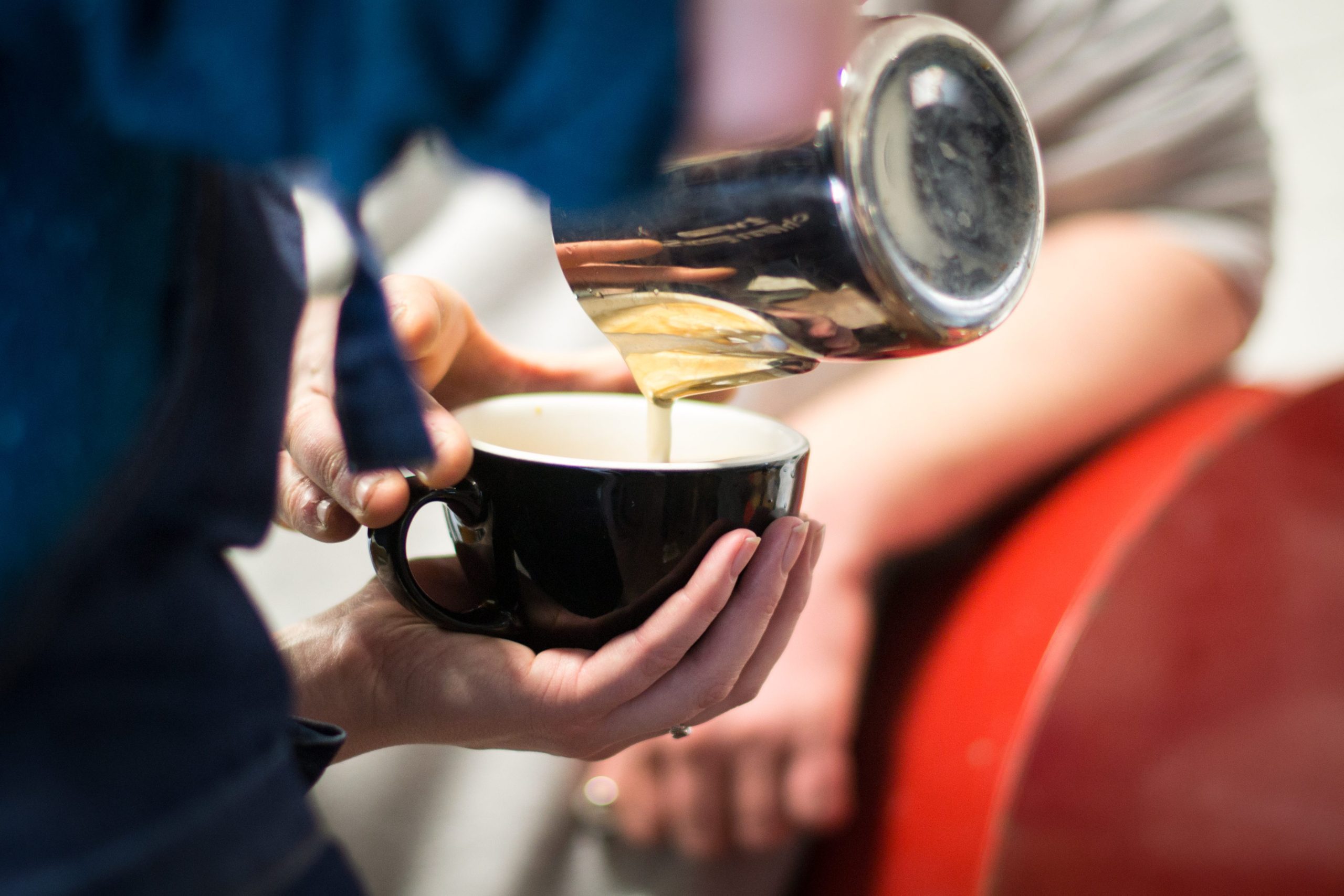 Pouring steamed milk into a black latte cup 