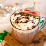 peppermint mocha topped with cream sits on wooden coasters besides green and silver toffees