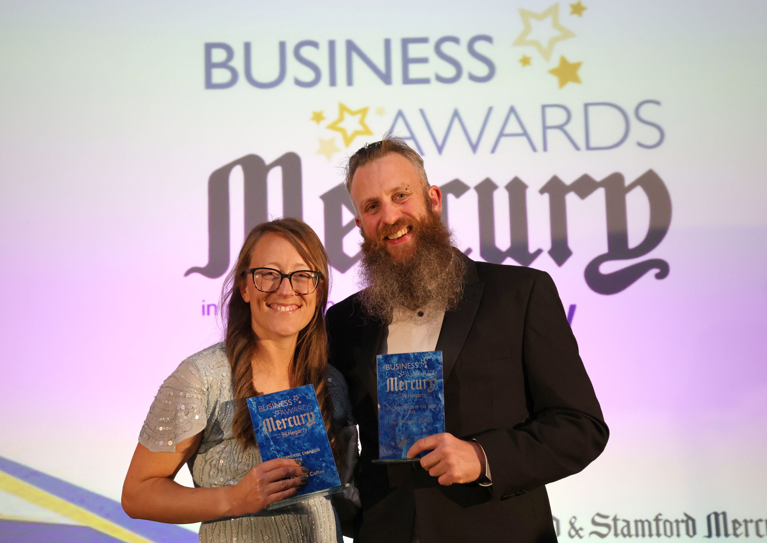 Andy and Laura from Two Chimps Coffee holding two awards, Environmental Champion and Small Business of the Year, at the 2024 Rutland and Stamford Mercury Business Awards