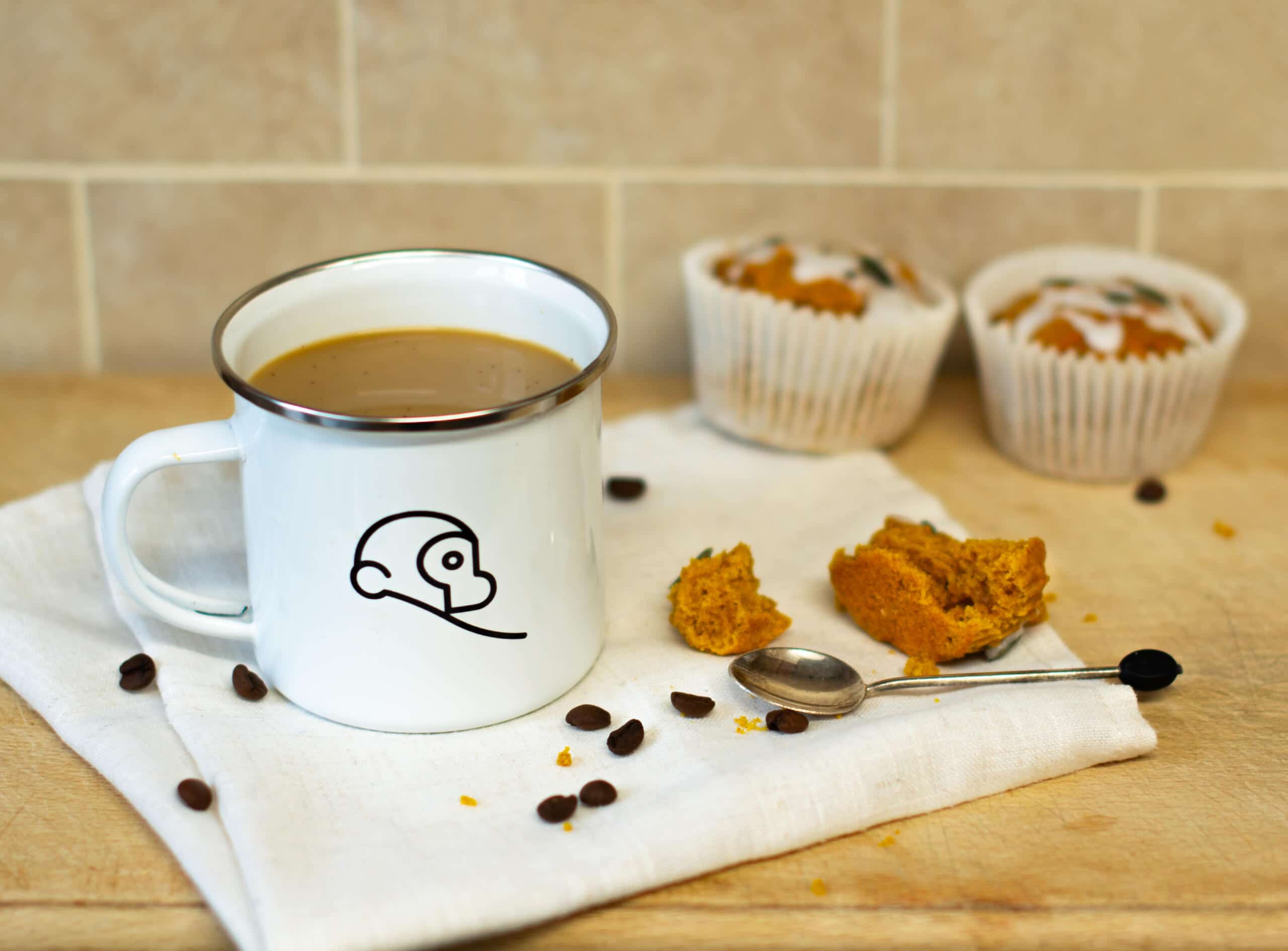 Pumpkin spice coffee in Two Chimps mug in front of two pumpkin muffins and beside a teaspoon and one half-eaten muffin