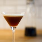 a cocktail glass with espresso martini and liquor in the background