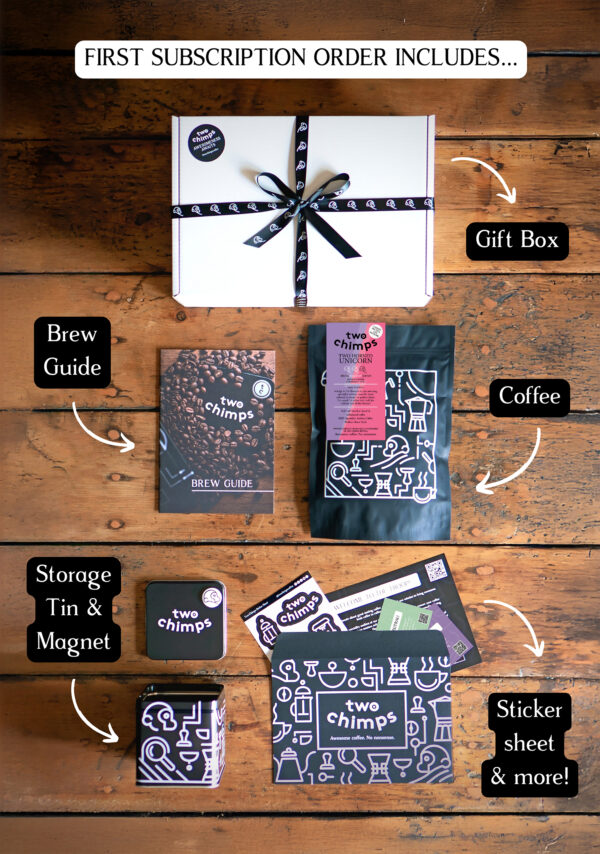 An image of a Two Chimps Coffee subscription box with the items included in it such as the brew guide, the storage tin & magnet and the coffee bag