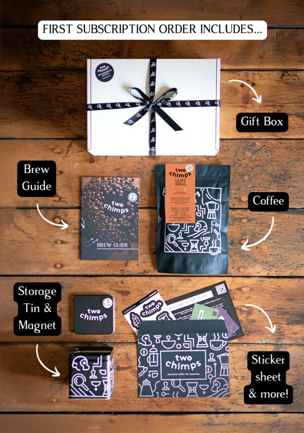 An image of a Two Chimps Coffee subscription box with the items included in it such as the brew guide, the storage tin & magnet and the coffee bag