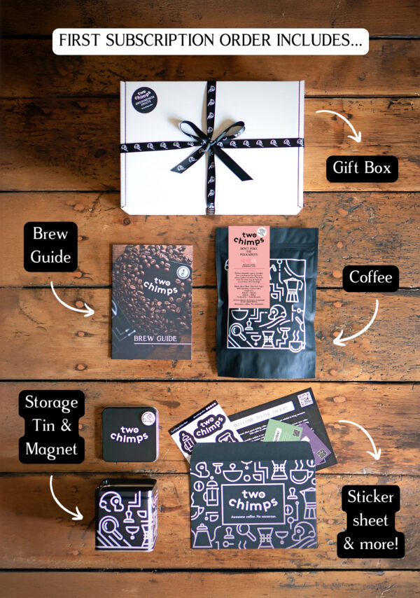 An image of a Two Chimps Coffee subscription box with the items included in it such as the brew guide, the storage tin & magnet and the coffee bag
