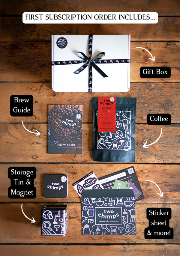 An image of a Two Chimps Coffee subscription box with the items included in it such as the brew guide, the storage tin & magnet and the coffee bag