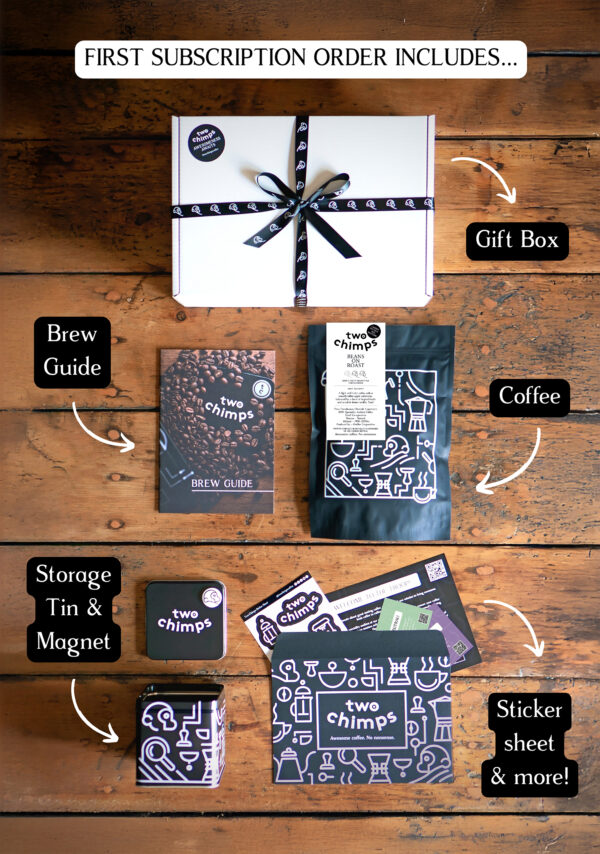 An image of a Two Chimps Coffee subscription box with the items included in it such as the brew guide, the storage tin & magnet and the coffee bag