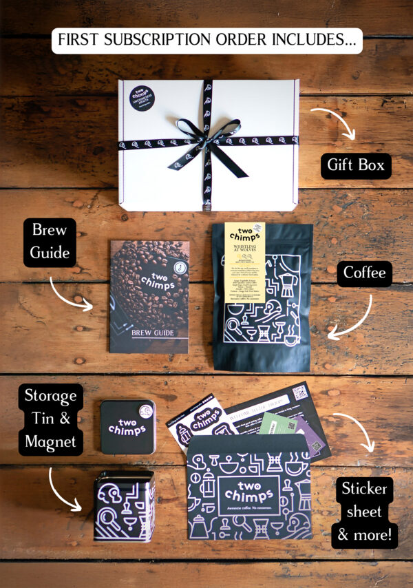 An image of a Two Chimps Coffee subscription box with the items included in it such as the brew guide, the storage tin & magnet and the coffee bag