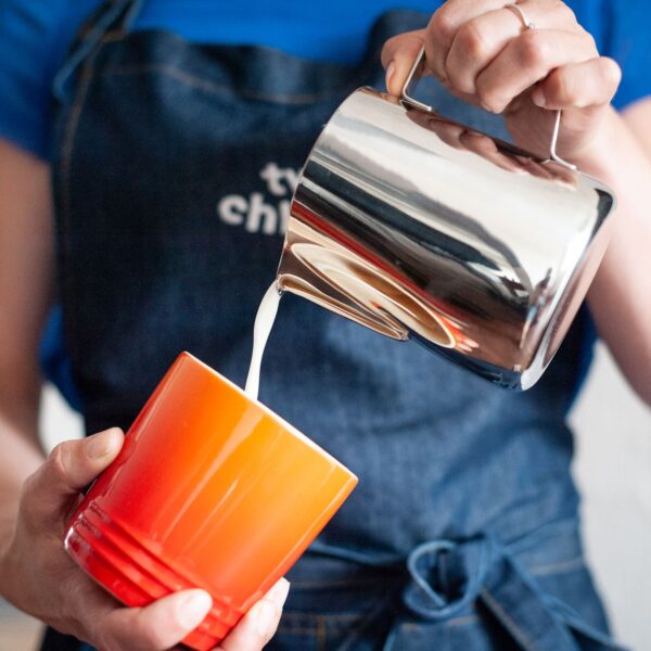 two chimps barista pouring milk from a jug into a cup