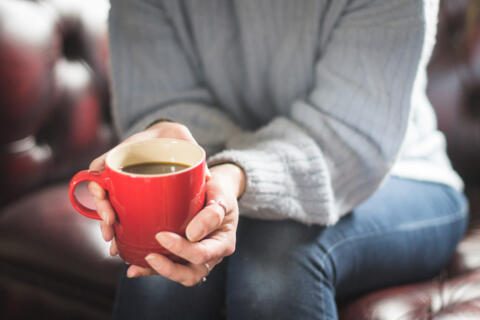 woman with grey jumper holding a red mug of tea