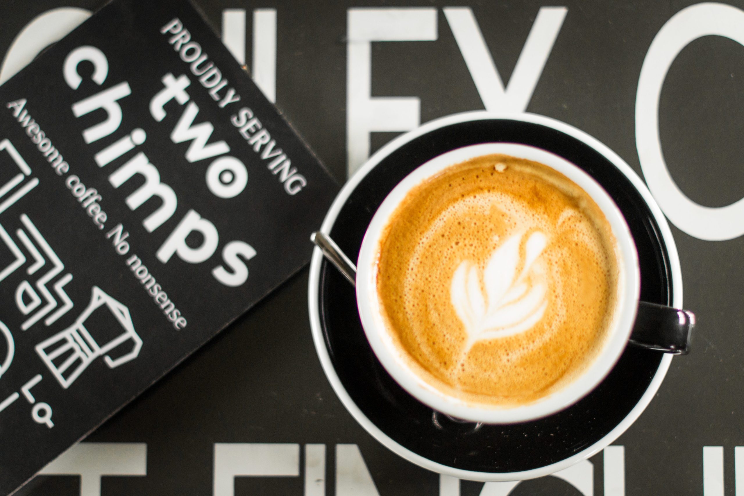 Latte in a black cup with Two Chimps Coffee advertising board