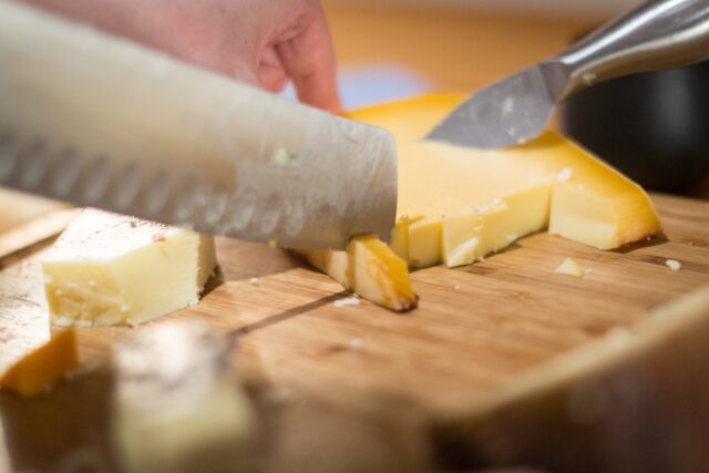 Cutting a piece of cheddar with a knife from a cheese board selection 