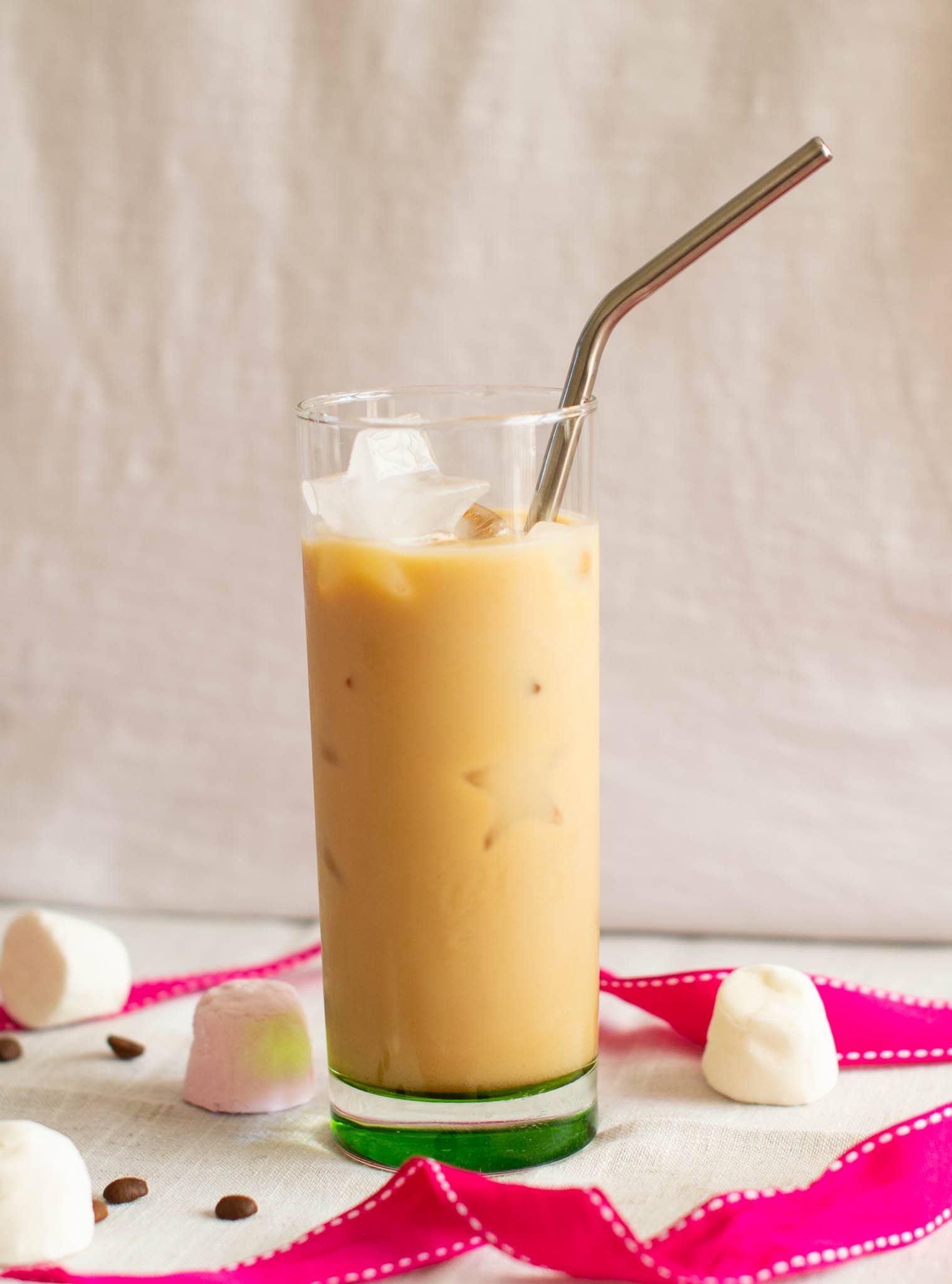 Vanilla iced latte with straw beside pink ribbon, marshmallows and coffee beans