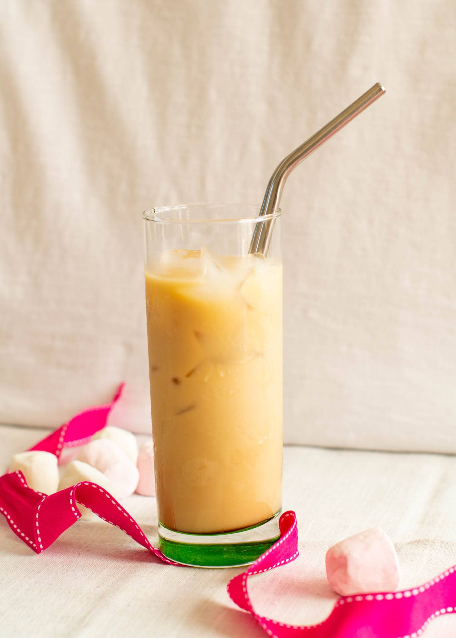 Vanilla iced latte with straw beside pink ribbon and marshmallows