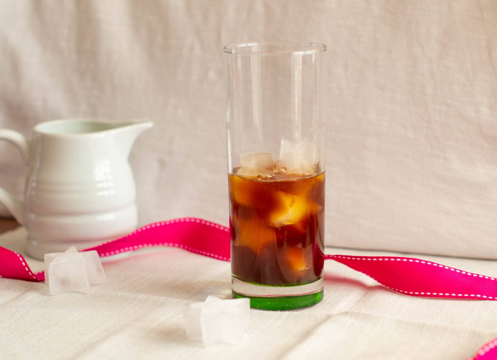 Glass with ice and coffee beside milk jug and pink ribbon