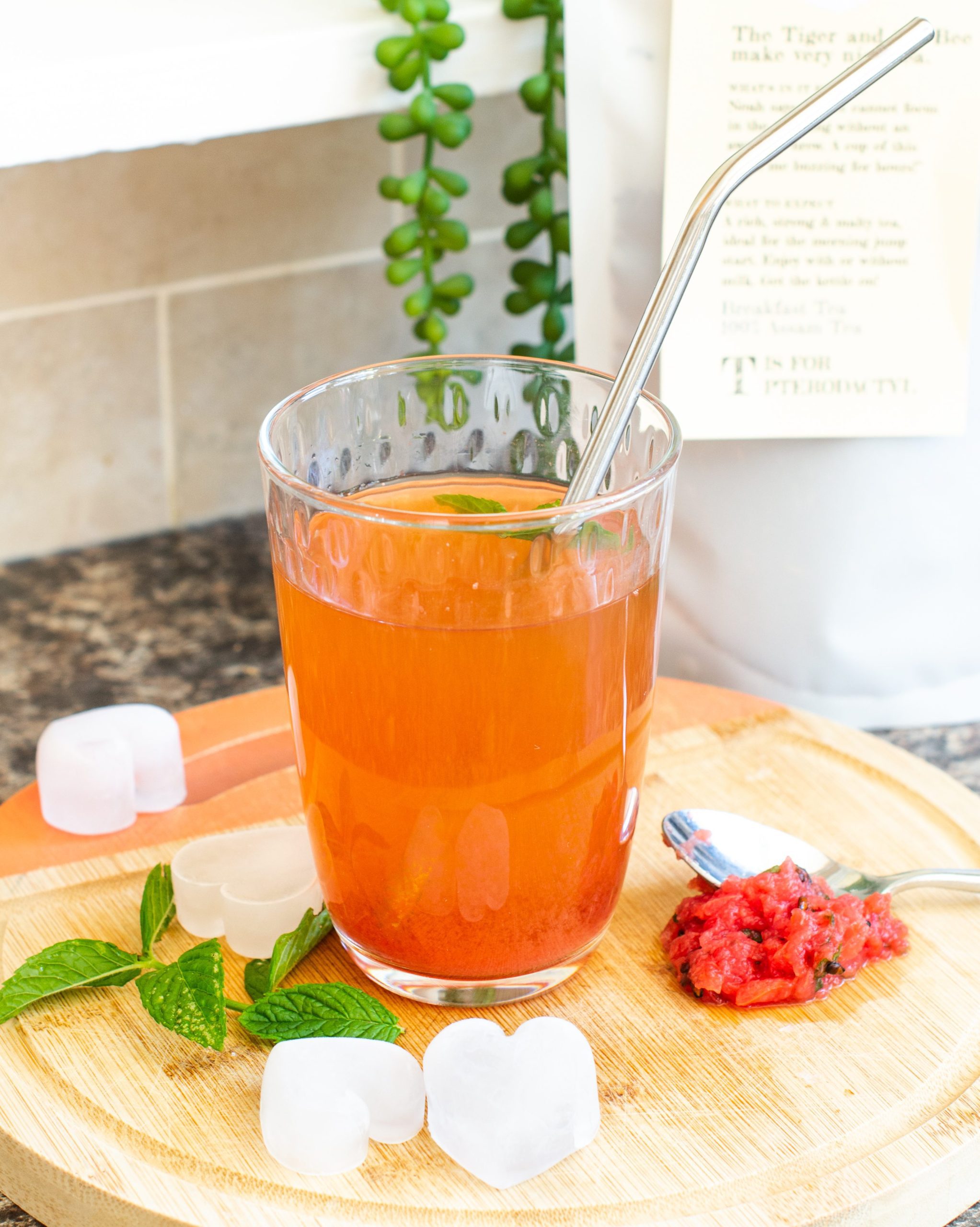 Glass of watermelon iced tea on chopping board with a bag of loose leaf black tea from Two Chimps