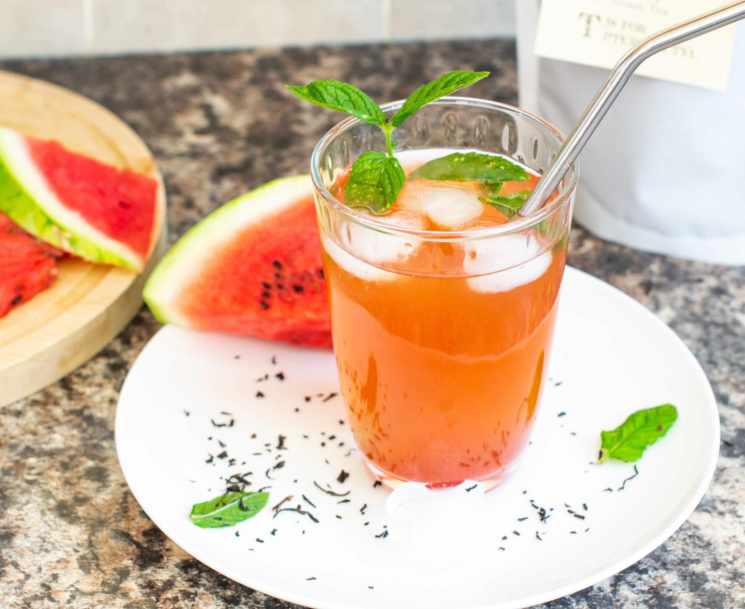 Glass of homemade watermelon iced tea on a white plate with watermelon wedges and mint leaves