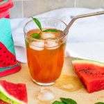 Glass of iced watermelon tea on a chopping board with ice, watermelon wedges and watermelon print lunchbag