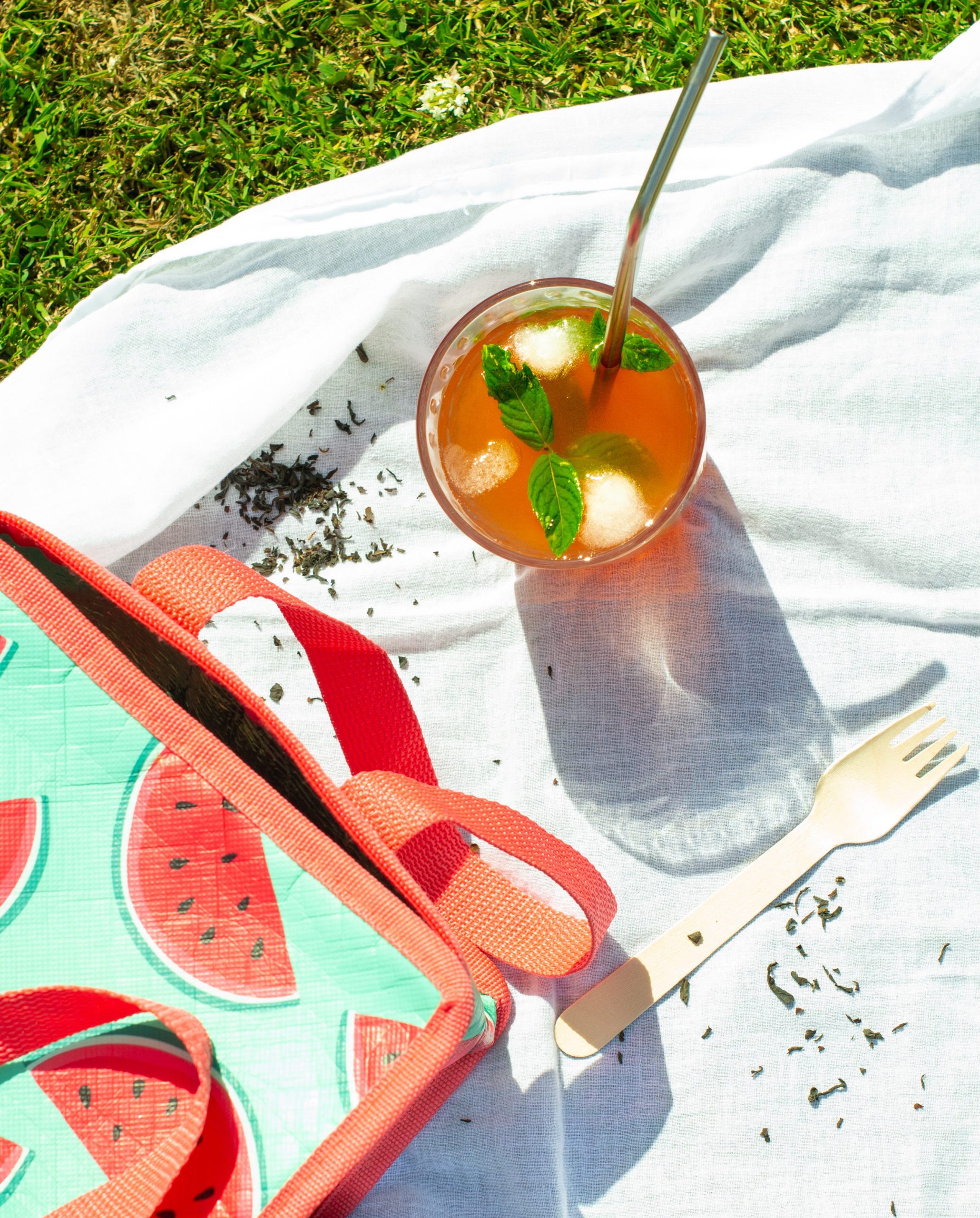 looking down on watermelon iced tea on white picnic sheet with watermelon lunch bag