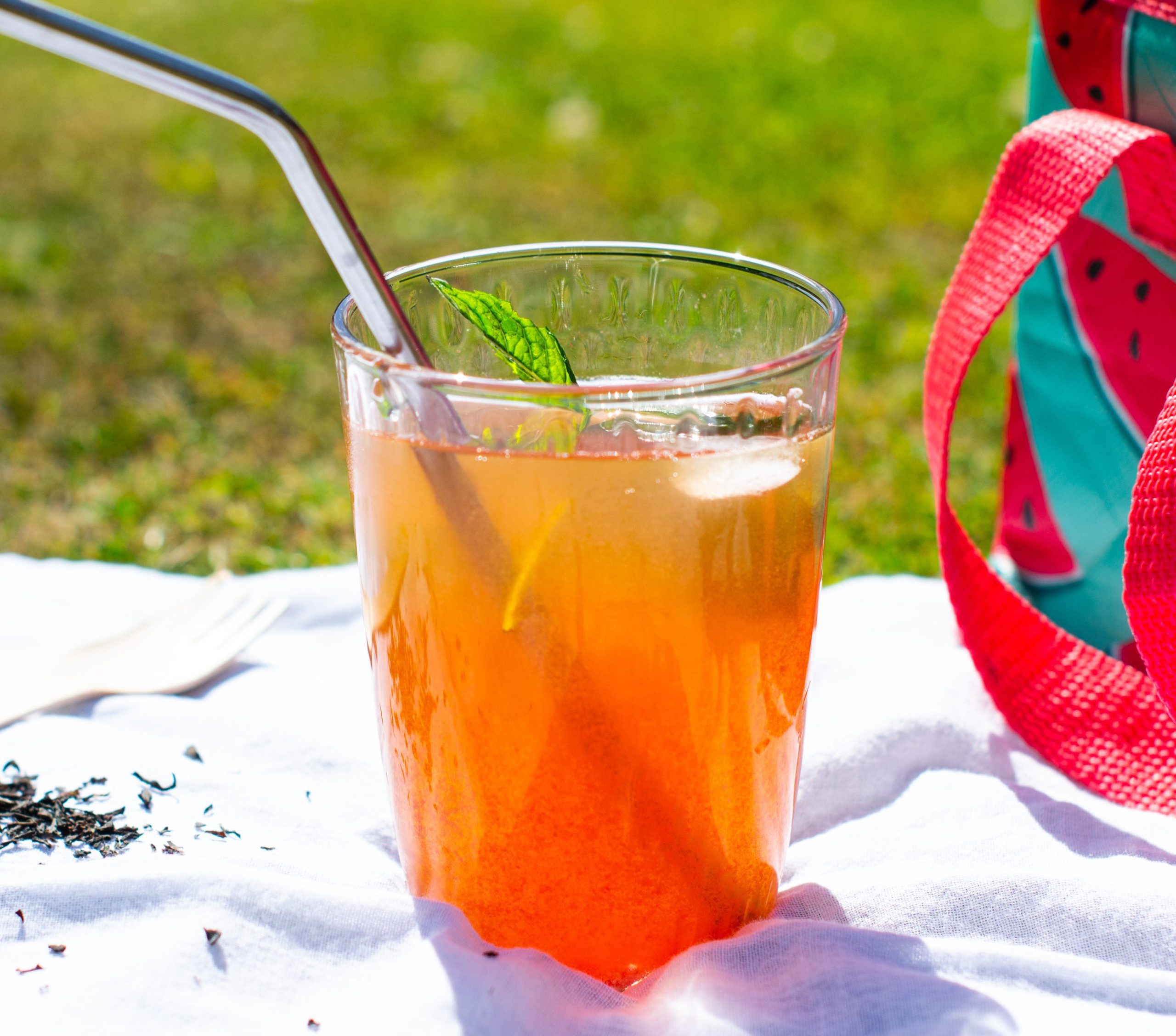 Glass of watermelon iced tea sits on white picnic sheet on the grass