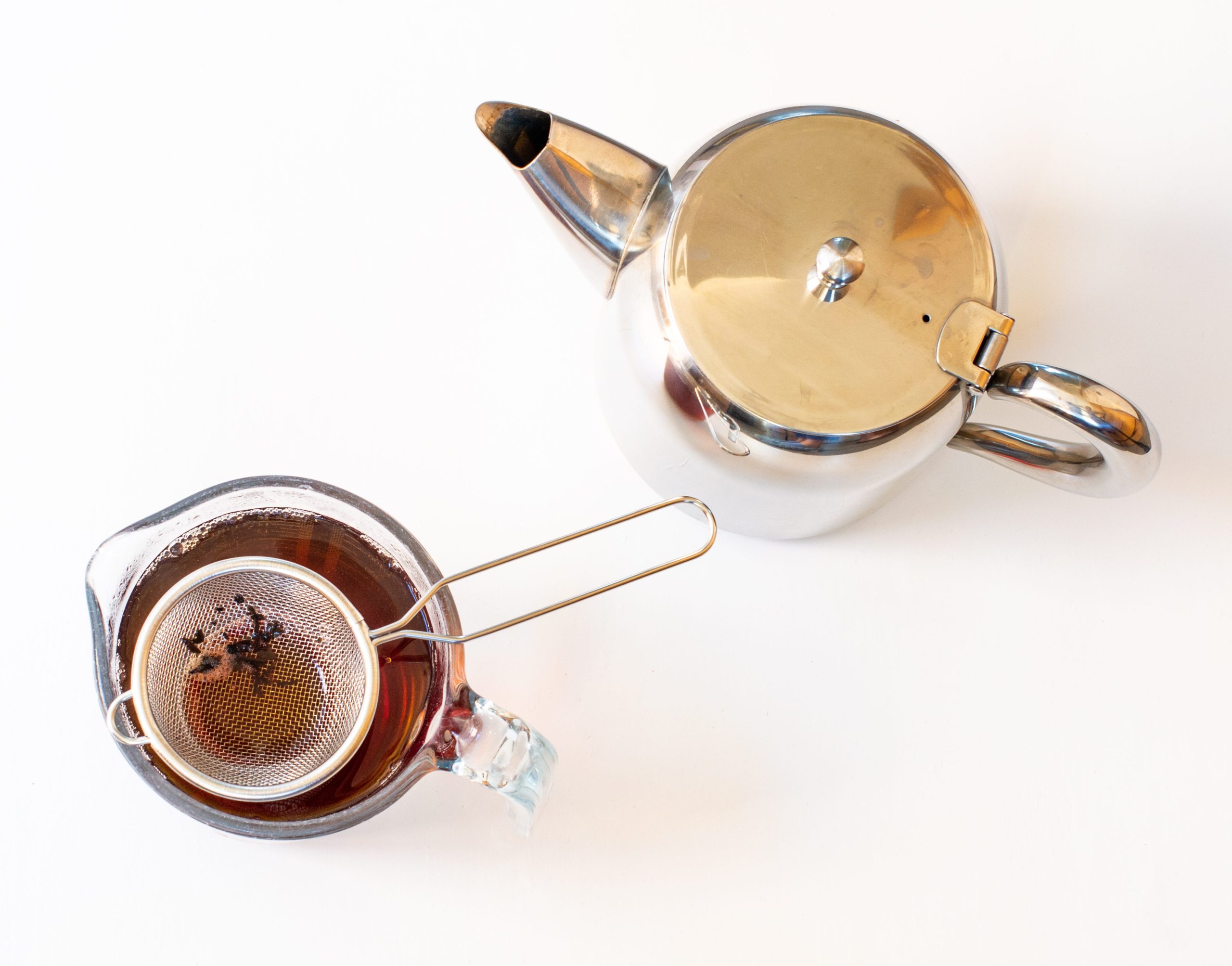 Looking down on a metal teapot and a measuring jug with strained loose leaf tea in