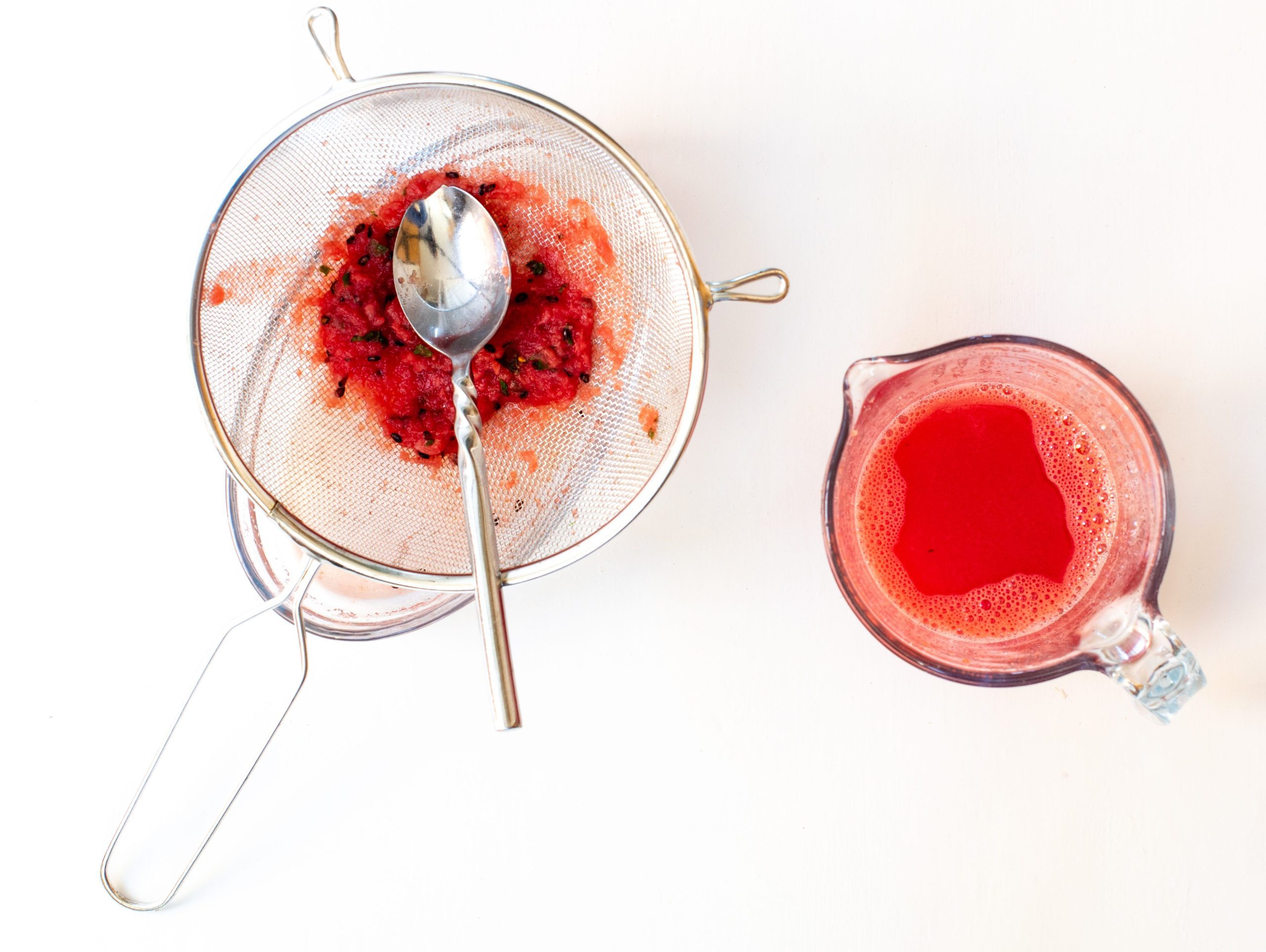 Straining watermelon juice through a sieve with a spoon
