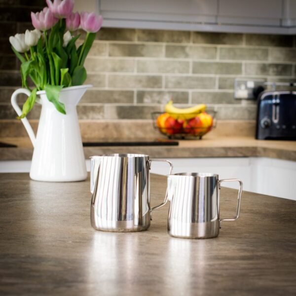 two unboxed milk steaming jugs in different sizes on a kitchen worktop
