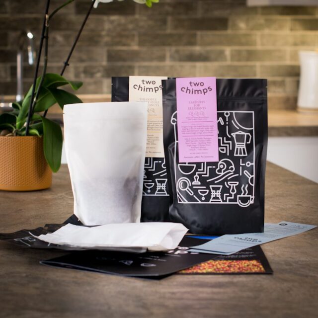 two bags of two chimps coffee with two bags of unroasted coffee beans and roasting guide on a kitchen worktop