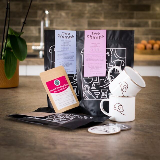 two bags of two chimps coffee,one bag of hot chocolate flakes,drinking spice,two enamel two chimps mugs and two chimp coasters all on a kitchen worktop