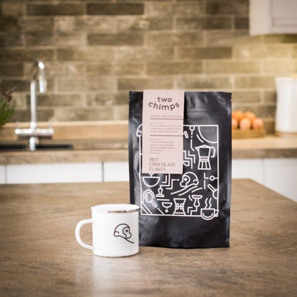 a bag of two chimps hot chocolate flakes with a two chimps enamel mug on a kitchen worktop