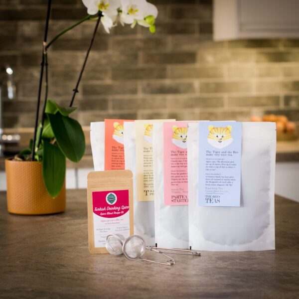 four bags of loose leaf tea with a drinking spice pouch and a tea infuser on a kitchen worktop